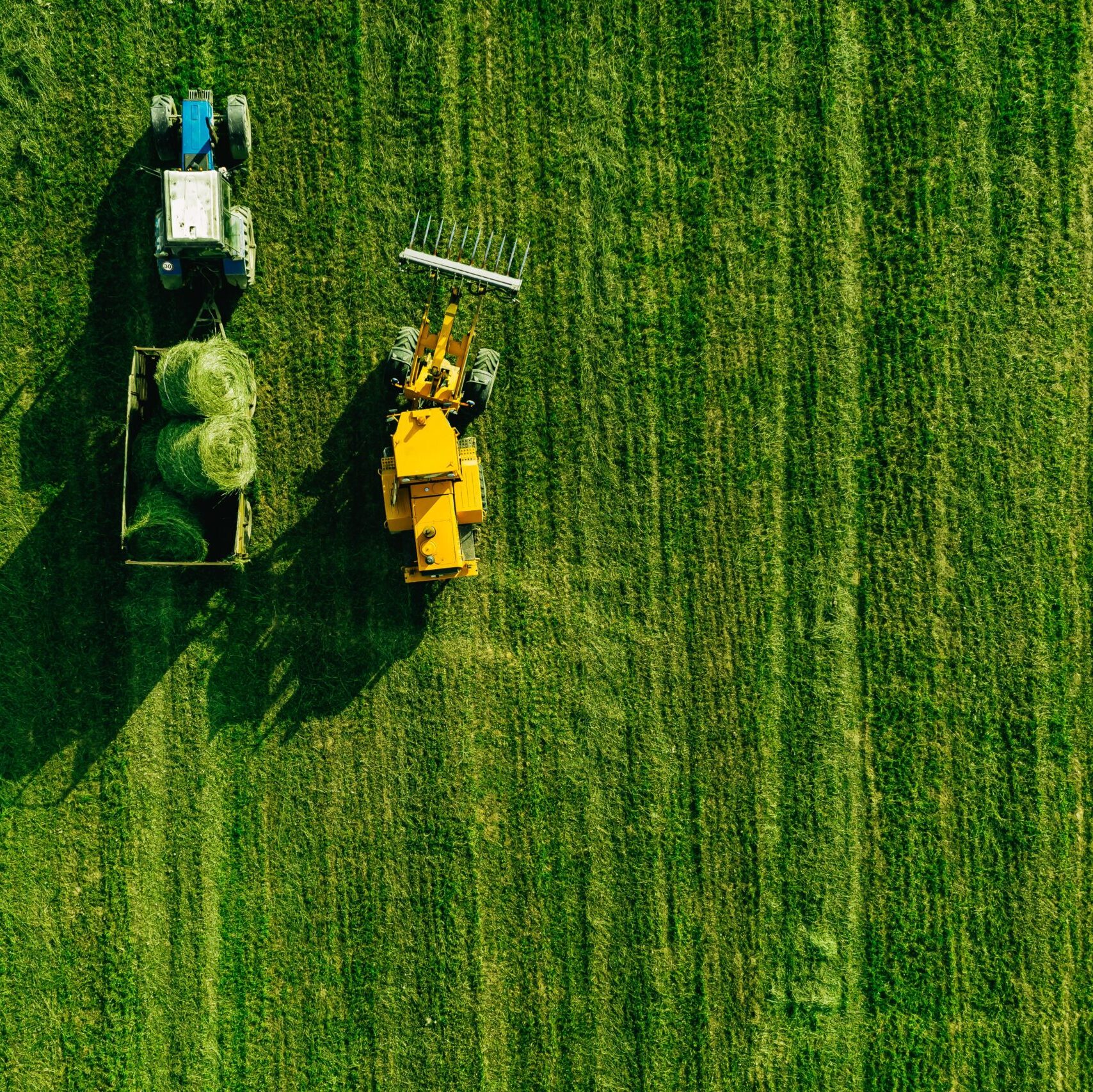 Aerial view of green grass harvest field with tractor moving hay bale